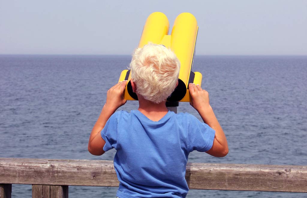 A boy looking at the sea through big binoculars.
